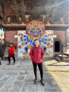 Jennifer in front of the detailed wood carvings and lord Bhairava mural at Chandeshwari Temple
